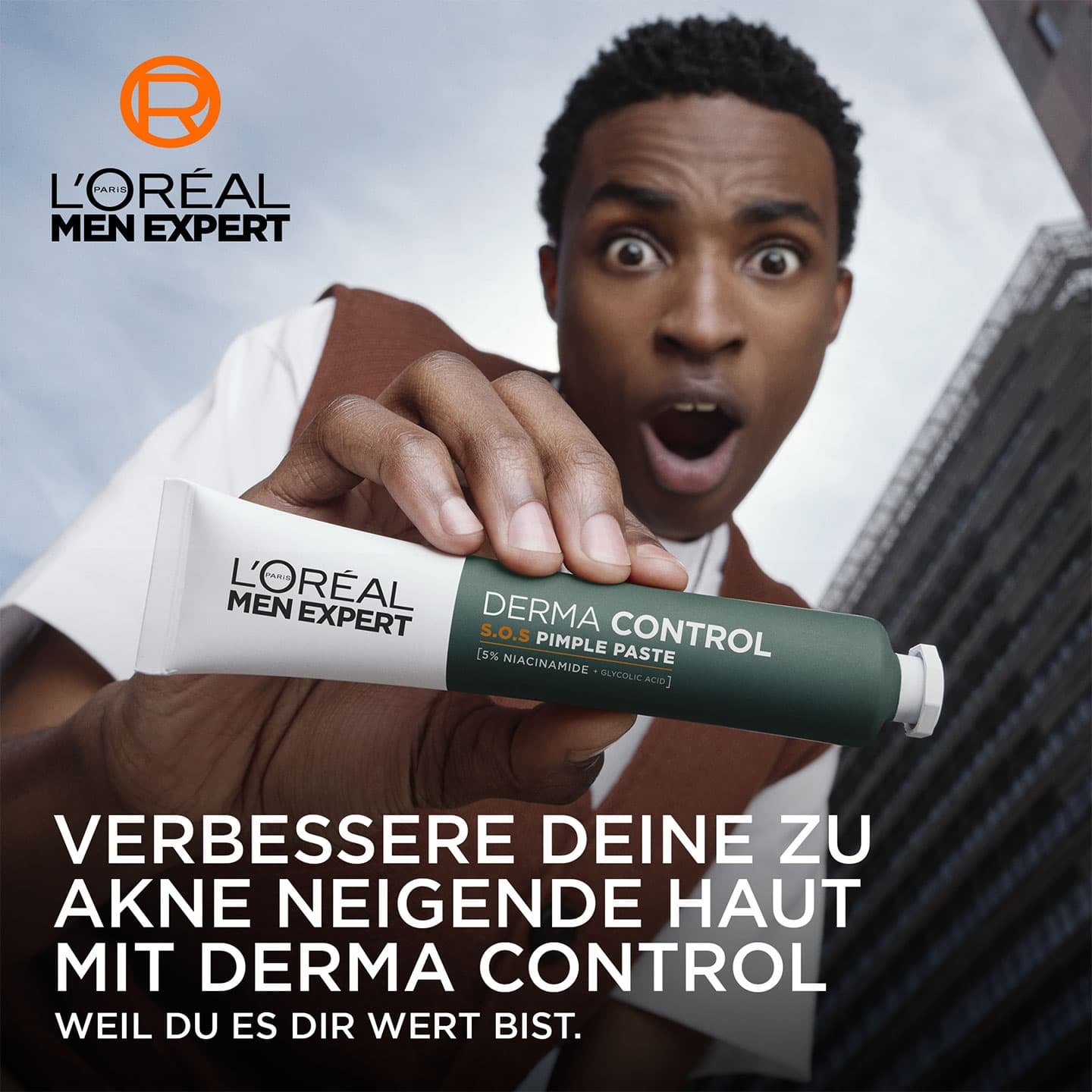 Ein junger Mann hält verwundert die L'Oréal Paris SOS 2-in-1 Anti-Pickel-Paste in seiner rechten Hand